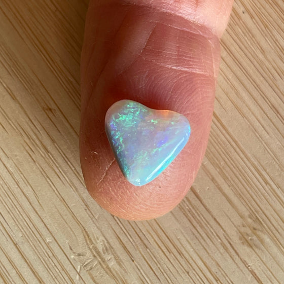 2.05 heart shaped crystal opal, this small bright heart has bright flashes of green, there is a darker line on one side.
