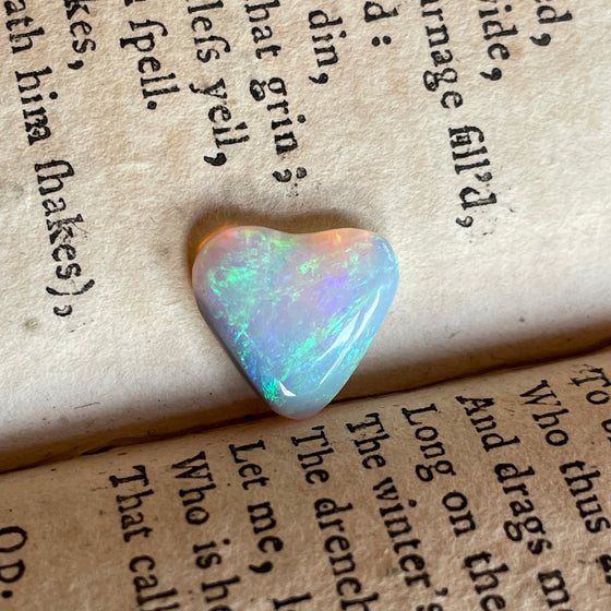 2.05 heart shaped crystal opal, this small bright heart has bright flashes of green, there is a darker line on one side.