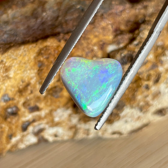 2.05 heart shaped crystal opal, this small bright heart has bright flashes of green, there is a darker line on one side.
