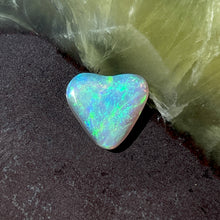  2.05 heart shaped crystal opal, this small bright heart has bright flashes of green, there is a darker line on one side. The heart shows a blue surface when out of bright light.